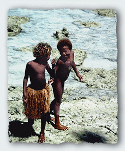 Two kids walk on the reef at low tide just off the raised platform of the village. 