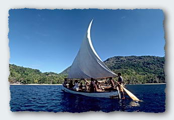 A PNG sailing canoe closes on the Moira as she lays at anchor in front of the village.